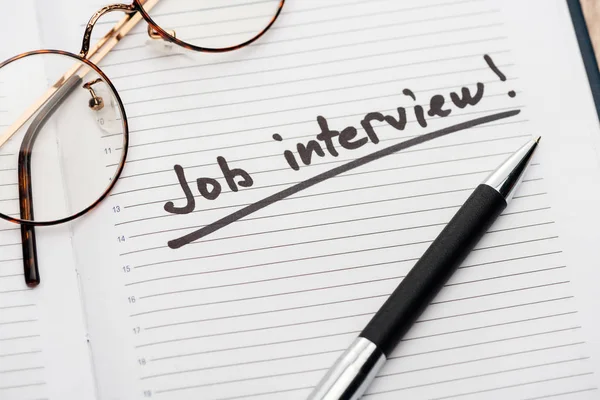 Notebook with pen, glasses and job interview black lettering — Stock Photo