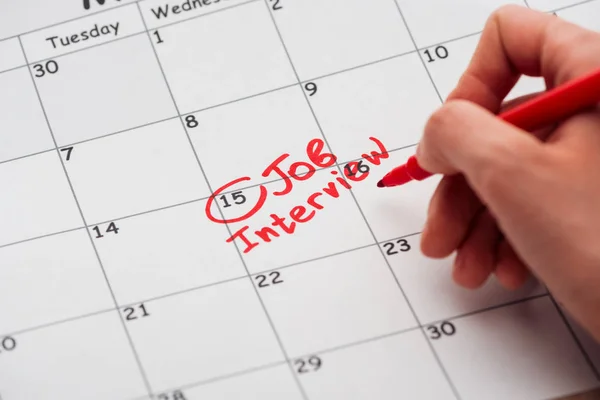 Partial view of man writing with red marker on print calendar with job interview lettering — Stock Photo