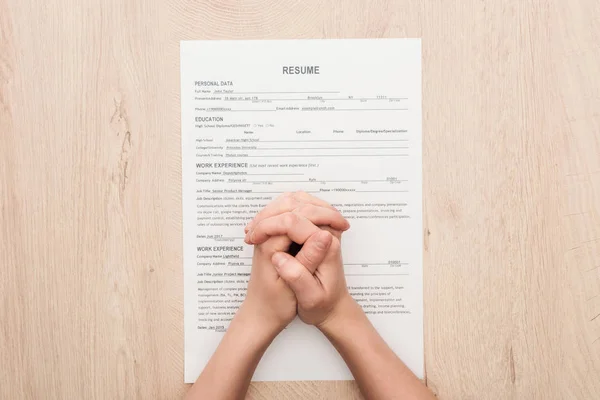 Partial view of recruiter holding clenched hands on resume template on wooden table — Stock Photo