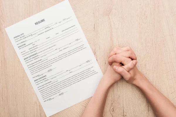 Cropped view of recruiter holding clenched hands near resume template on wooden table — Stock Photo