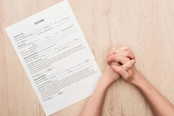 Vista cortada do recrutador segurando as mãos apertadas perto do modelo de currículo na mesa de madeira — Fotografia de Stock