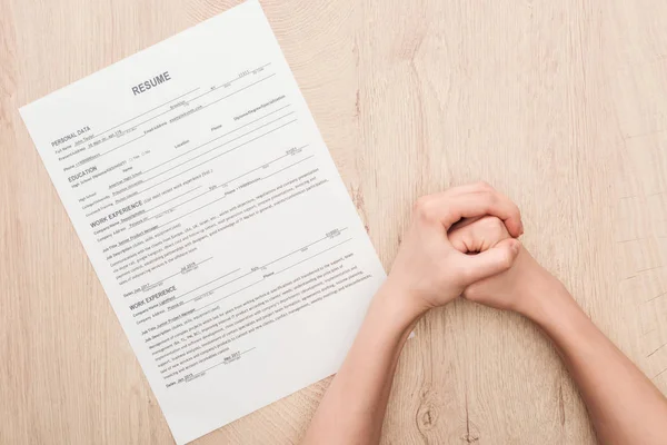 Partial view of recruiter holding clenched hands near resume template on wooden table — Stock Photo
