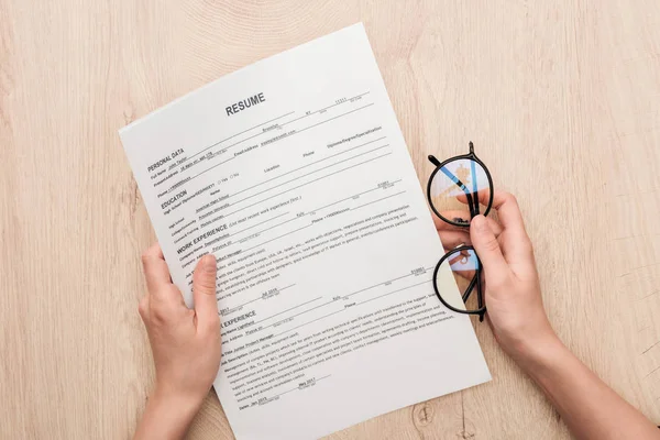 Partial view of recruiter holding resume template and glasses on wooden table — Stock Photo