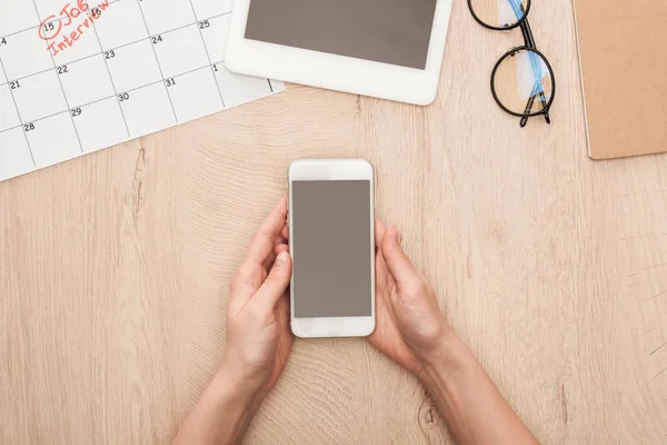 Vista parcial del reclutador sosteniendo smartphone con pantalla en blanco en el lugar de trabajo - foto de stock