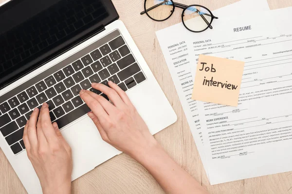 Cropped view of recruiter typing on laptop keyboard near glasses, resume templates and sticky note with job interview lettering — Stock Photo