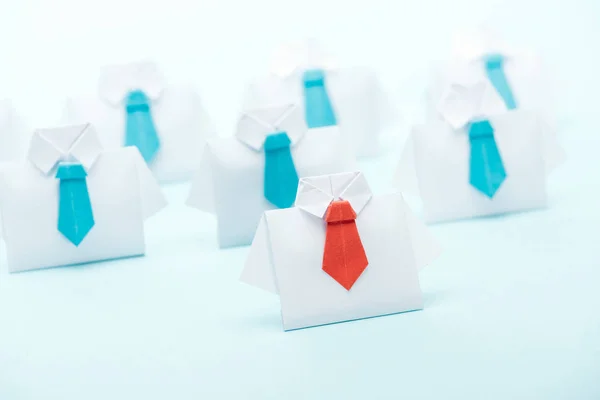 Selective focus of origami white shirts with blue ties with one red on blue background, leadership concept — Stock Photo