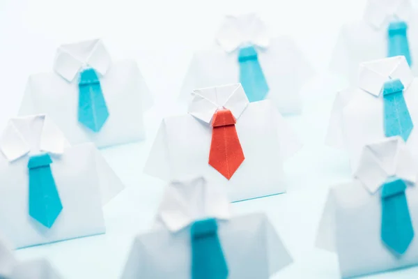 Selective focus of origami white shirts with blue ties with one red on blue background, think different concept — Stock Photo