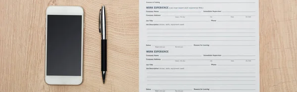 Panoramic shot of pen, smartphone with blank screen and resume template on wooden surface — Stock Photo