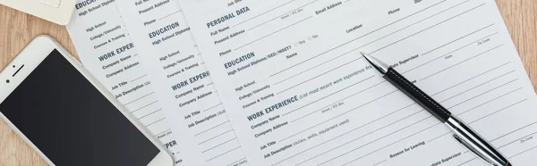 Panoramic shot of pen, smartphone with blank screen and resume templates on wooden surface — Stock Photo