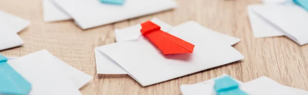 Panoramic shot of origami white shirts with blue ties with one red on wooden surface — Stock Photo