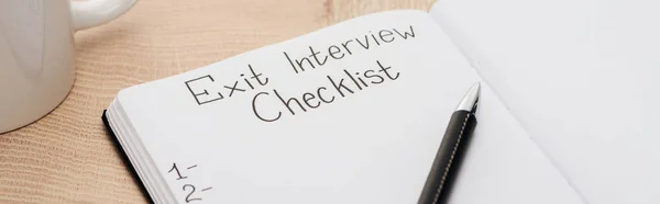 Panoramic shot of notebook with exit interview checklist lettering and numbers on wooden table with pen — Stock Photo