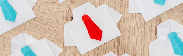 Colpo panoramico di origami camicie bianche con legami blu con uno rosso su sfondo di legno, pensare concetto diverso — Foto stock