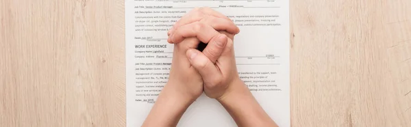 Panoramic shot of recruiter holding clenched hands on resume template on wooden table — Stock Photo