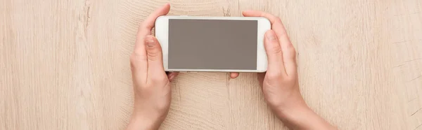 Panoramic shot of woman holding smartphone with blank screen at wooden table — Stock Photo