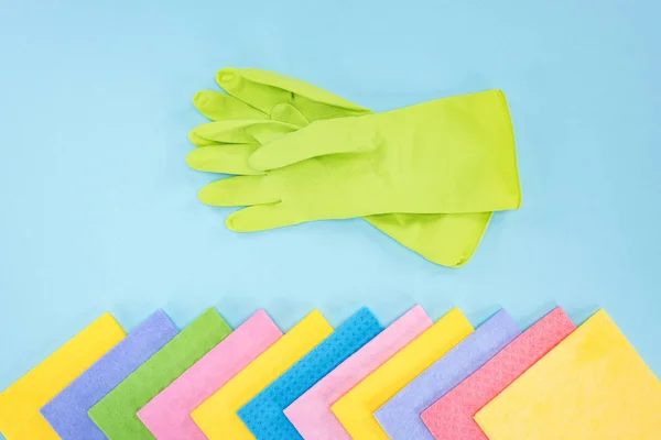 Vista superior de guantes de goma verde y trapos multicolores sobre fondo azul - foto de stock