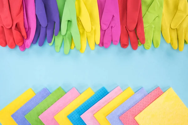 Top view of multicolored bright rubber gloves and rags on blue background with copy space — Stock Photo
