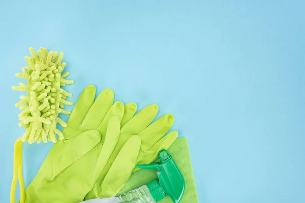 Вид зверху на зелені гумові рукавички, губку, ганчірку та пляшку спрею з миючим засобом на синьому фоні з місцем для тексту — стокове фото
