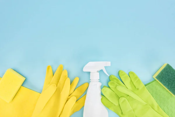 Ansicht von gelben und grünen Gummihandschuhen, Schwämmen, Lumpen und Sprühflasche mit Waschmittel auf blauem Hintergrund mit Kopierraum — Stockfoto