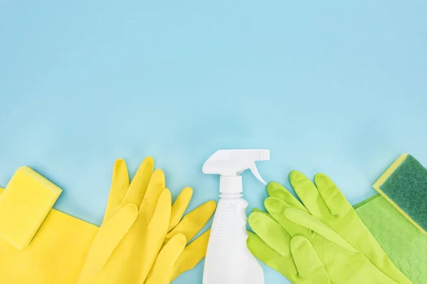 Vue de dessus des gants en caoutchouc jaune et vert, des éponges, des chiffons et du flacon pulvérisateur avec détergent sur fond bleu avec espace de copie — Photo de stock