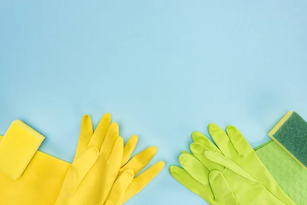 Vista dall'alto di guanti di gomma gialli e verdi, spugne, stracci su sfondo blu con spazio copia — Foto stock