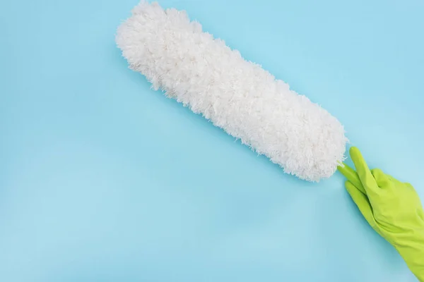 Cropped view of cleaner in green rubber glove holding duster on blue background — Stock Photo