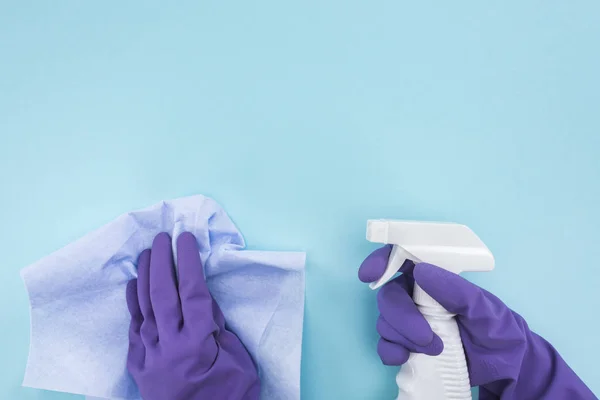 Vista ritagliata di detergente in guanti di gomma viola con straccio e bottiglia spray con detergente su sfondo blu — Foto stock
