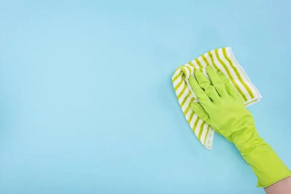 Cropped view of cleaner in green rubber glove holding striped rag on blue background — Stock Photo