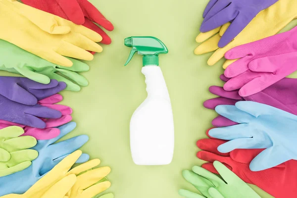 Вид зверху різнокольорових гумових рукавичок навколо пляшки спрею з миючим засобом на зеленому фоні — стокове фото