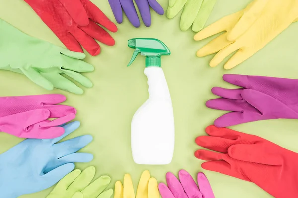 Top view of multicolored rubber gloves in circle around spray bottle with detergent on green background — Stock Photo