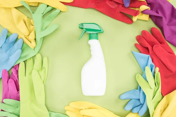 Top view of multicolored rubber gloves in circle with spray bottle with detergent in center on green background — Stock Photo