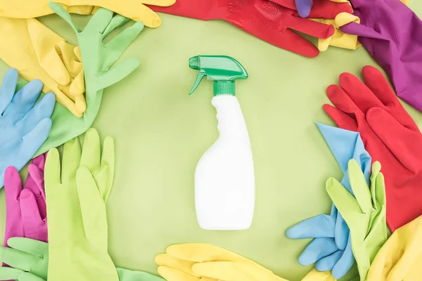 Vista superior de guantes de goma multicolores en círculo con botella de spray con detergente en el centro sobre fondo verde - foto de stock