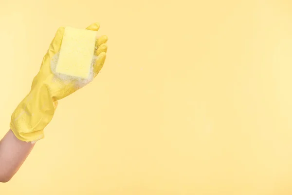 Vista cortada de limpador em luva de borracha amarela segurando esponja com bolhas no fundo amarelo — Fotografia de Stock