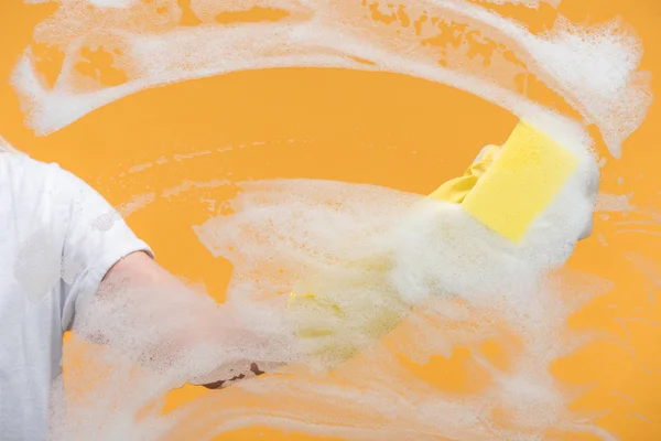 Vista cortada de limpador em luva de borracha limpeza de vidro com esponja sobre fundo laranja — Fotografia de Stock