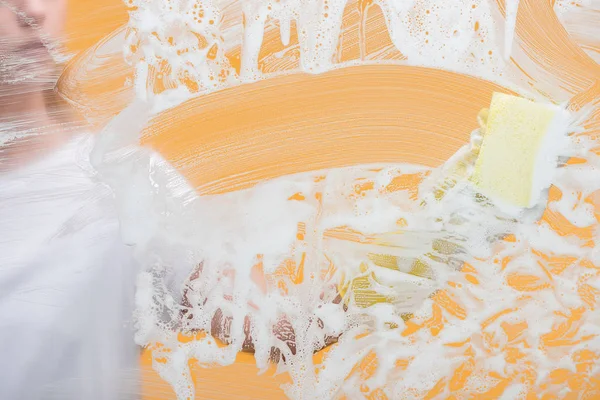 Cropped view of young woman in rubber glove with sponge cleaning glass covered with foam — Stock Photo