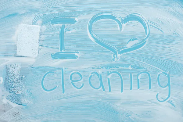Abgeschnittene Ansicht von Reiniger mit Schwamm in der Nähe Ich liebe Reinigung handgeschriebenen Schriftzug auf Glas mit weißem Schaum auf blauem Hintergrund — Stockfoto