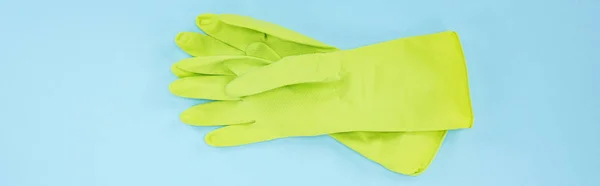 Panoramic shot of bright green rubber gloves on blue background — Stock Photo