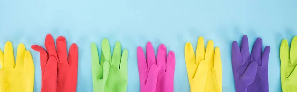 Plano panorámico de guantes de goma multicolores en fila sobre fondo azul - foto de stock