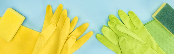 Panoramic shot of yellow and green rubber gloves, sponges, rags on blue background — Stock Photo