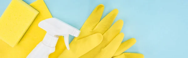 Plano panorámico de guantes de goma amarilla, esponja, trapo y spray sobre fondo azul con espacio para copiar — Stock Photo