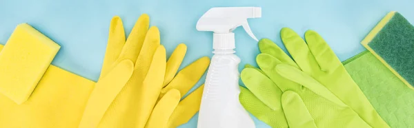 Prise de vue panoramique de gants en caoutchouc jaune et vert, éponges, chiffons et vaporisateur avec détergent sur fond bleu — Photo de stock