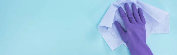 Panoramic shot of cleaner in purple rubber glove holding rag on blue background — Stock Photo