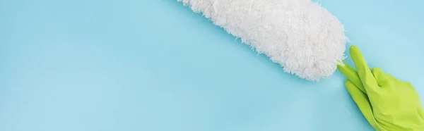 Panoramic shot of cleaner in green rubber glove holding duster on blue background — Stock Photo