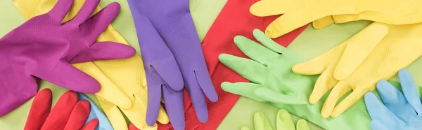 Panoramic shot of messy scattered multicolored rubber gloves on green background — Stock Photo