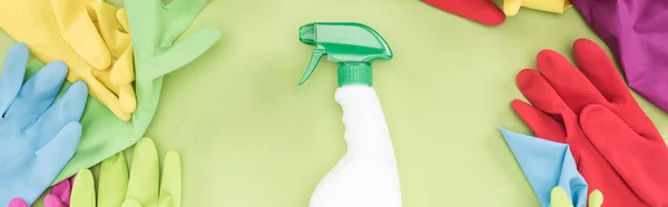 Panoramic shot of rubber gloves in circle around spray bottle with detergent on green background — Stock Photo