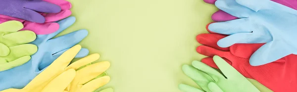 Panoramic shot of multicolored rubber gloves on green background with copy space — Stock Photo
