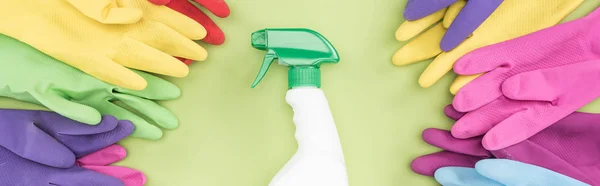 Panoramic shot of bright rubber gloves in circle around spray bottle with detergent on green background — Stock Photo