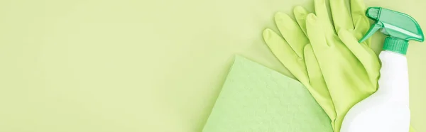 Plano panorámico de guantes de goma verde, trapo y botella de spray sobre fondo verde - foto de stock