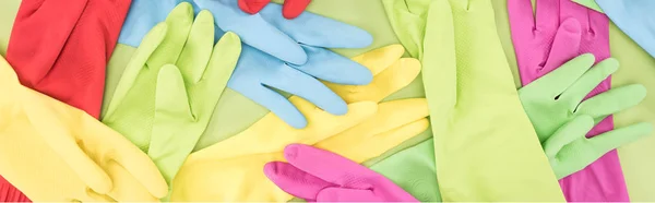 Panoramic shot of scattered bright multicolored rubber gloves on green background — Stock Photo