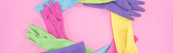 Plano panorámico de guantes de goma multicolores dispuestos en círculo sobre fondo rosa - foto de stock