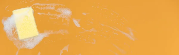 Panoramic shot of yellow sponge with foam on orange background — Stock Photo